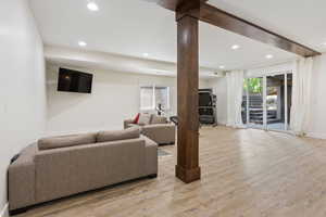 Living room with decorative columns, light hardwood / wood-style flooring, and beam ceiling