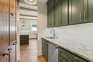 Kitchen with decorative backsplash, green cabinets, dishwasher, light hardwood / wood-style flooring, and sink