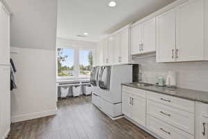 Clothes washing area featuring sink, washing machine and dryer, cabinets, and dark wood-type flooring