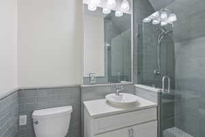 Bathroom with decorative backsplash, tile walls, a shower with door, toilet, and vanity