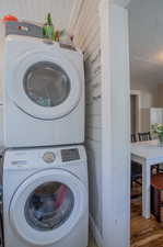 Clothes washing area featuring a textured ceiling, stacked washer / dryer, and hardwood / wood-style floors