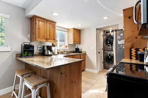 Kitchen featuring kitchen peninsula, plenty of natural light, stacked washer and dryer, and stone counters