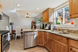 Kitchen with light tile patterned floors, appliances with stainless steel finishes, sink, and light stone counters