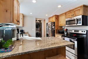 Kitchen featuring kitchen peninsula, stacked washer and clothes dryer, appliances with stainless steel finishes, and light stone countertops