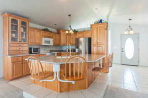 Kitchen featuring lofted ceiling, stainless steel refrigerator, stove, light tile patterned floors, and an island with sink