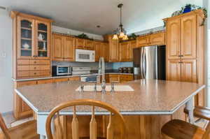 Kitchen featuring range, a kitchen island with sink, sink, stainless steel refrigerator with ice dispenser, and decorative light fixtures