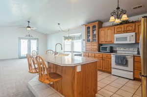 Kitchen with lofted ceiling, ceiling fan with notable chandelier, white appliances, light carpet, and sink