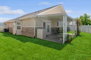 Rear view of house with cooling unit, a lawn, and a patio area