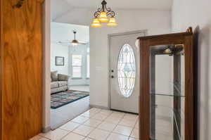 Carpeted entryway featuring ceiling fan with notable chandelier and vaulted ceiling