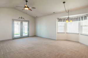 Spare room with ceiling fan with notable chandelier, vaulted ceiling, and light colored carpet