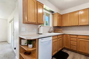 Kitchen with decorative backsplash, white dishwasher, sink, and light colored carpet