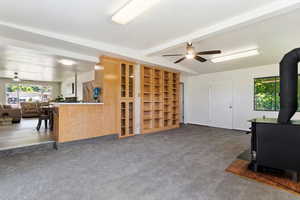 Living room featuring vaulted ceiling with beams, a wood stove, carpet flooring, and ceiling fan