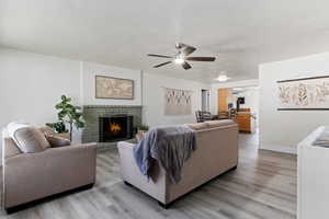 Living room with ceiling fan, light hardwood / wood-style flooring, a textured ceiling, and a brick fireplace