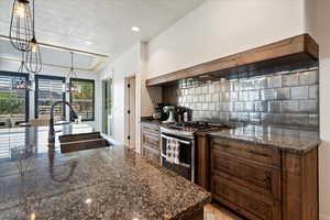 Kitchen featuring a textured ceiling, hanging light fixtures, backsplash, sink, and gas range oven