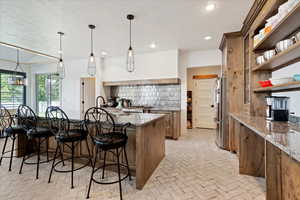 Kitchen with a kitchen bar, stainless steel fridge, stone countertops, decorative light fixtures, and tasteful backsplash