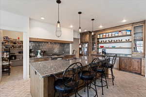 Kitchen featuring a large island with sink, hanging light fixtures, appliances with stainless steel finishes, sink, and backsplash