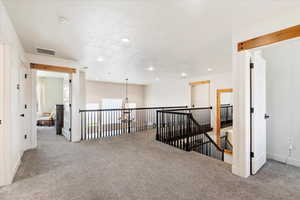 Empty room featuring carpet flooring, a textured ceiling, and an inviting chandelier