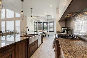 Kitchen with a textured ceiling, stainless steel appliances, dark stone countertops, decorative backsplash, and decorative light fixtures