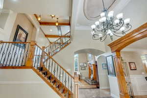 Stairs featuring a notable chandelier, crown molding, wood beams in ceiling, and a healthy amount of sunlight.