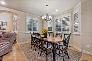 Tiled dining space featuring a notable chandelier, ornamental molding, and a healthy amount of sunlight