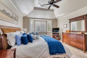 Carpeted bedroom with ceiling fan, ornamental molding, and a tray ceiling