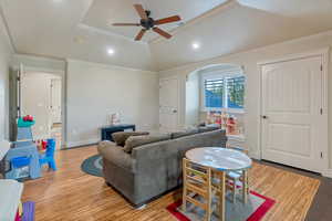 Living room with ceiling fan, crown molding, vaulted ceiling, and light hardwood / wood-style floors