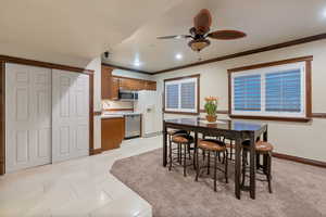 Dining space featuring ceiling fan, sink, light tile patterned flooring, and crown molding