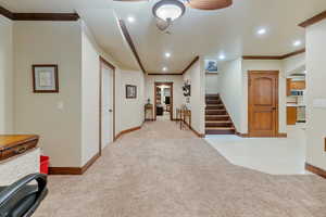 Basement landing and hallway to second basement family room, featuring ceiling fan, light colored carpet, and crown molding