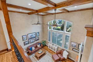 Living room with hardwood flooring, crown molding, beam ceiling, ceiling fan, and a high ceiling