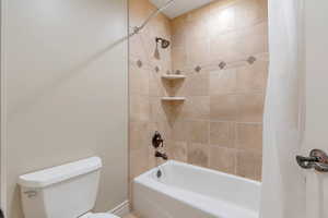 Bathroom featuring toilet and shower / bath combination with curtain