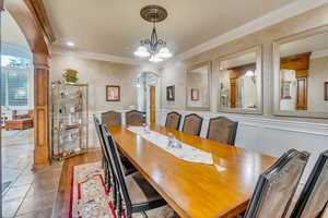 Tiled dining space featuring a notable chandelier, ornamental molding, and ornate columns