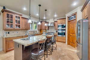 Kitchen featuring a center island with sink, appliances with stainless steel finishes, light tile patterned floors, two sinks, and vented hood