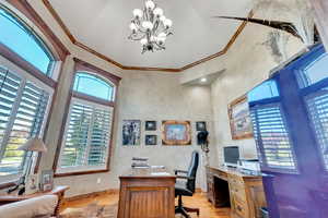 Home office featuring light wood-type flooring, a high ceiling, crown molding, and a chandelier