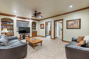 Carpeted living room with ceiling fan, ornamental molding, and built in features