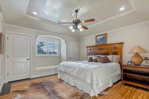 Bedroom featuring ceiling fan, a tray ceiling, ornamental molding, and light hardwood floors