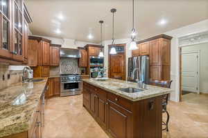 Kitchen featuring stainless steel appliances, a kitchen island with sink, custom exhaust hood, two sinks, and decorative backsplash