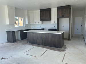 Kitchen with white cabinets, dark brown cabinetry, a center island, and a textured ceiling