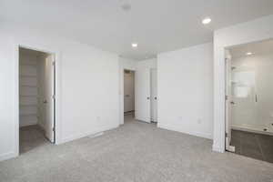 Unfurnished bedroom featuring a closet, connected bathroom, a spacious closet, and light colored carpet