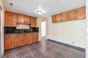 Kitchen featuring a textured ceiling, decorative backsplash, sink, dark tile patterned flooring, and dark stone counters