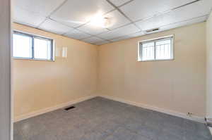 Basement with a paneled ceiling, dark tile patterned flooring, and a healthy amount of sunlight