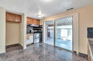 Kitchen with stainless steel electric stove, a textured ceiling, dark tile patterned flooring, and backsplash