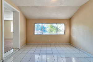 Another view of Bedroom #1, a Tiled empty room featuring a textured ceiling and lofted ceiling