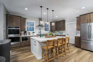 Kitchen with light hardwood / wood-style floors, wall chimney exhaust hood, a center island, decorative light fixtures, and stainless steel appliances