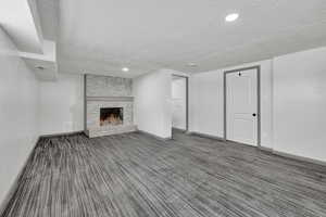 Unfurnished living room with a brick fireplace, a textured ceiling, and dark colored carpet