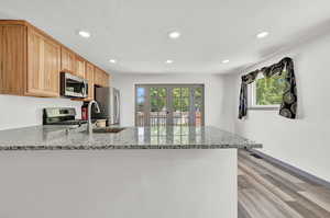 Kitchen with appliances with stainless steel finishes, light wood-type flooring, kitchen peninsula, and a wealth of natural light