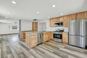 Kitchen featuring light stone countertops, stainless steel appliances, kitchen peninsula, and light hardwood / wood-style floors