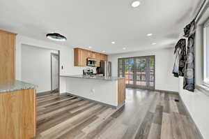 Kitchen featuring light hardwood / wood-style flooring, stainless steel appliances, kitchen peninsula, and light stone countertops