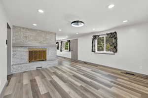 Unfurnished living room featuring wood-type flooring, a fireplace, brick wall, and a healthy amount of sunlight