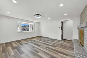 Unfurnished living room featuring wood-type flooring and a brick fireplace