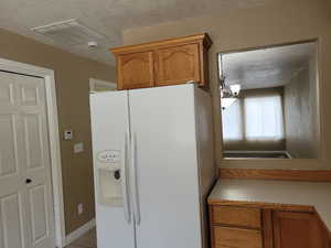 Kitchen featuring a textured ceiling, white fridge with ice dispenser, and light tile patterned flooring